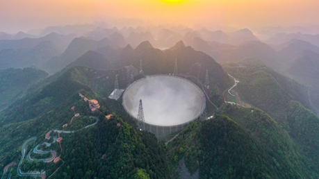 FAST radio telescope among green mountain ranges at sunset